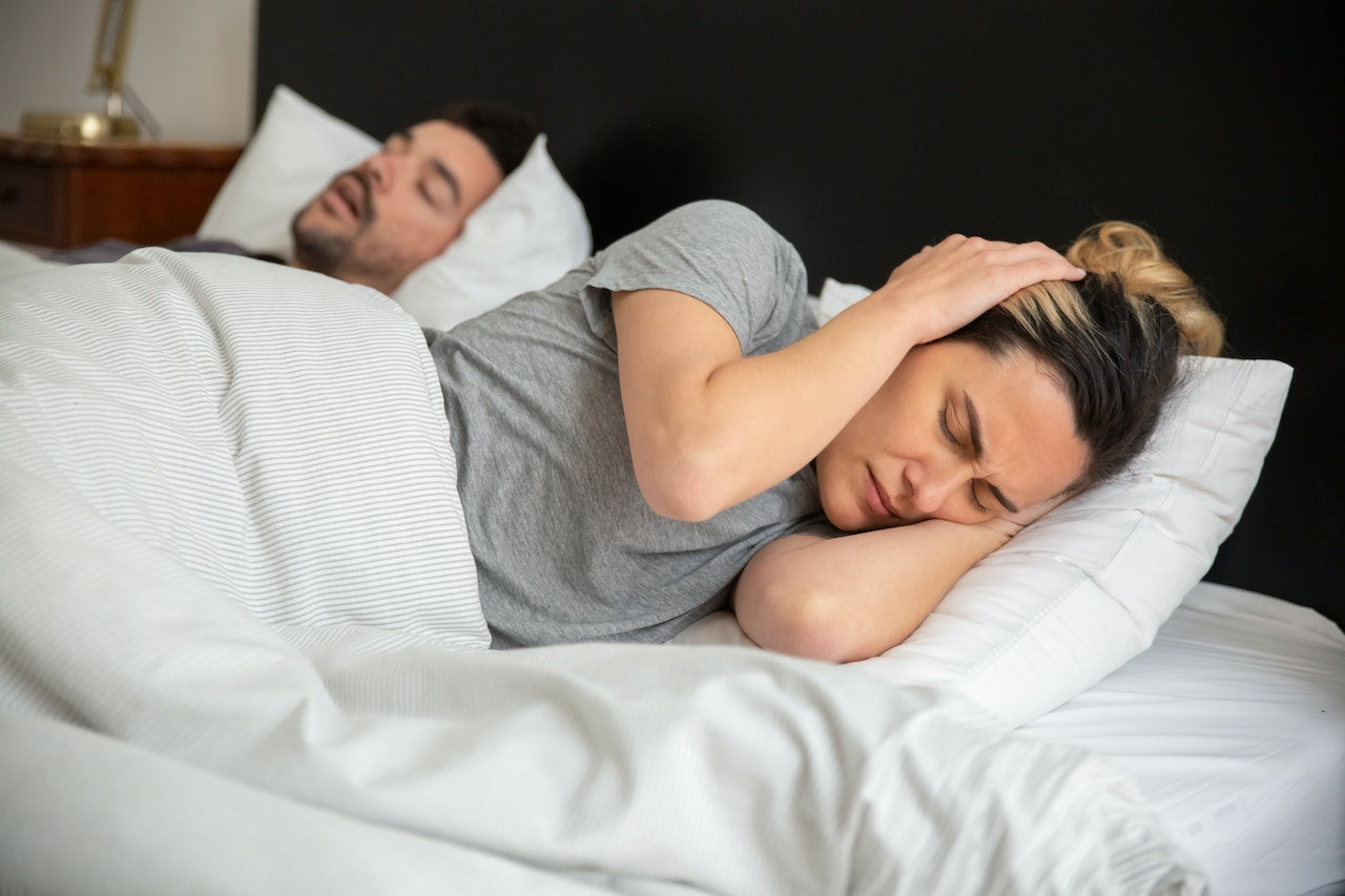 Man en vrouw slapen in bed, maar de vrouw heeft last van partner's gesnurk.